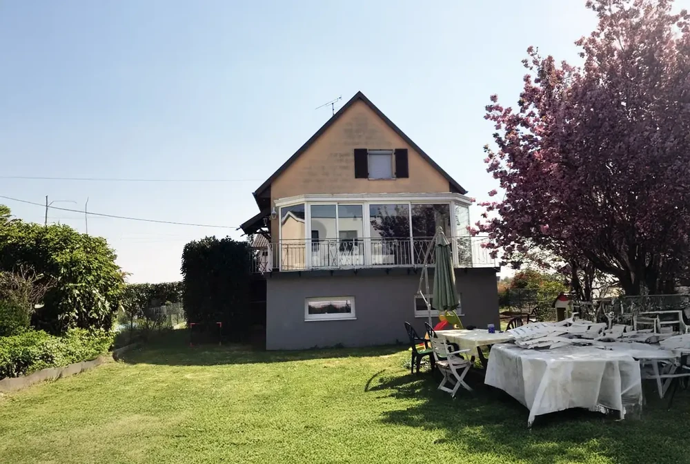 Maison contemporaine avec terrasse extérieure aménagée, tables et chaises modernes, végétation paysagée, éclairage crépusculaire