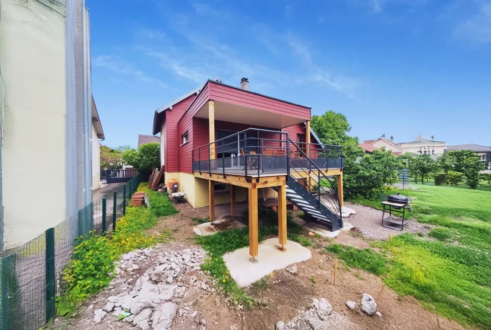 Maison contemporaine surélevée sur pilotis avec bardage rouge et structure bois apparent