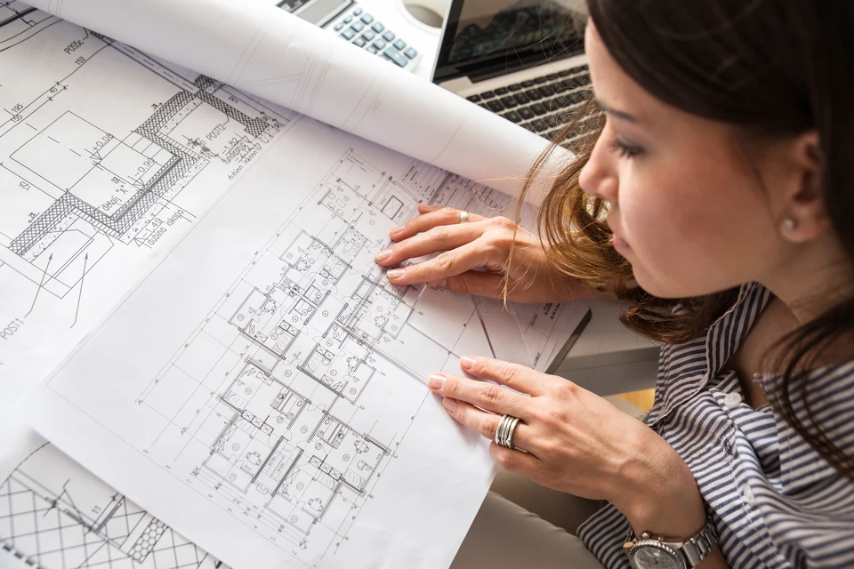 Femme architecte examinant des plans d'architecture détaillés sur une table de travail en intérieur