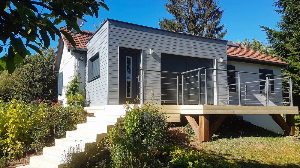 Extension contemporaine en bardage bois gris avec terrasse surélevée et garde-corps métalliques horizontaux