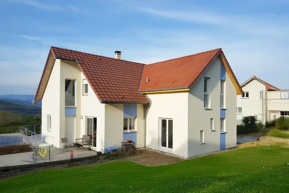 Maison individuelle moderne avec extension contemporaine, façade blanche aux volets rouges, toiture en tuiles terre cuite avec panneaux solaires